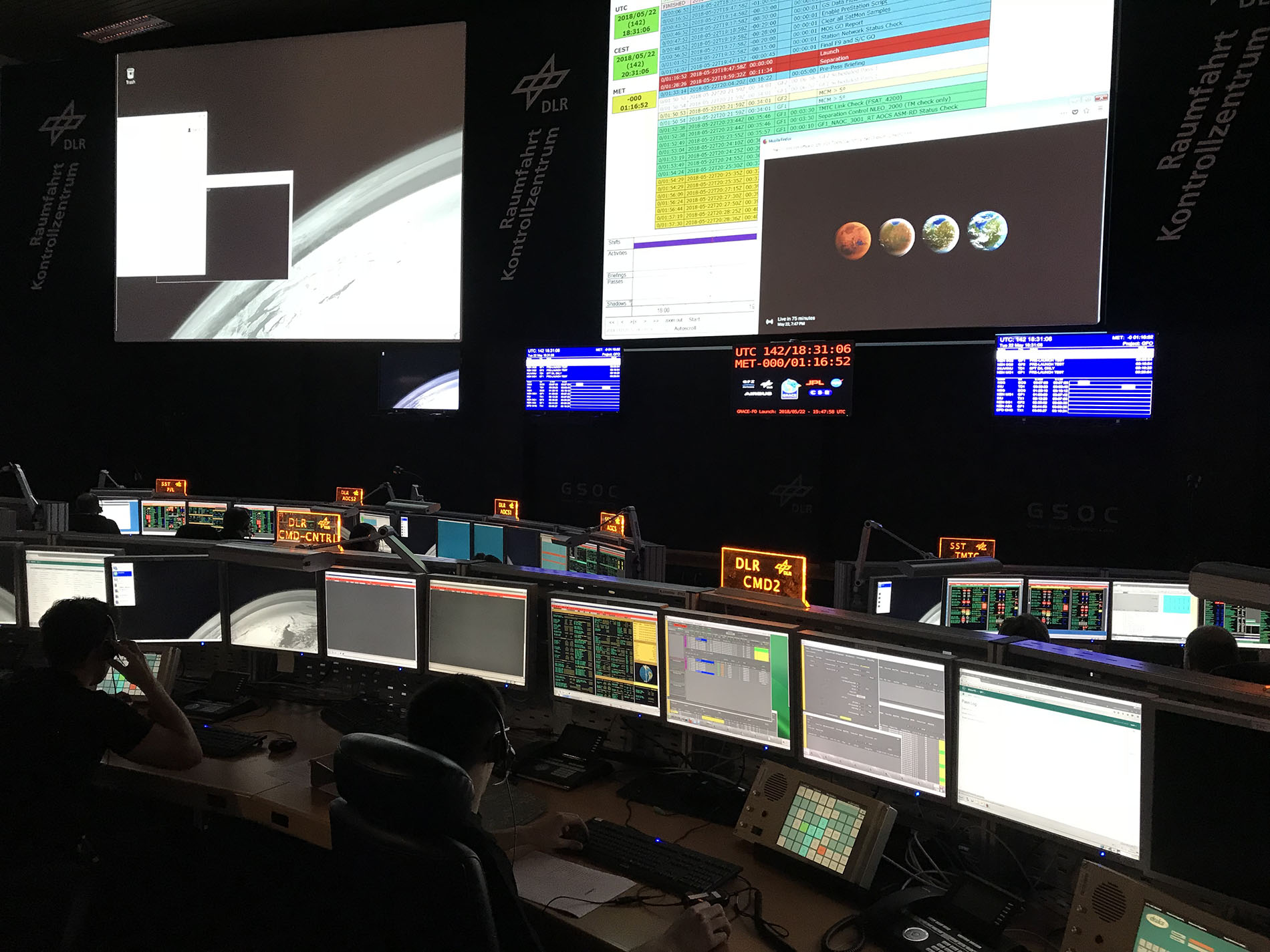 The darkened room of mission control is lighted by computer screens.