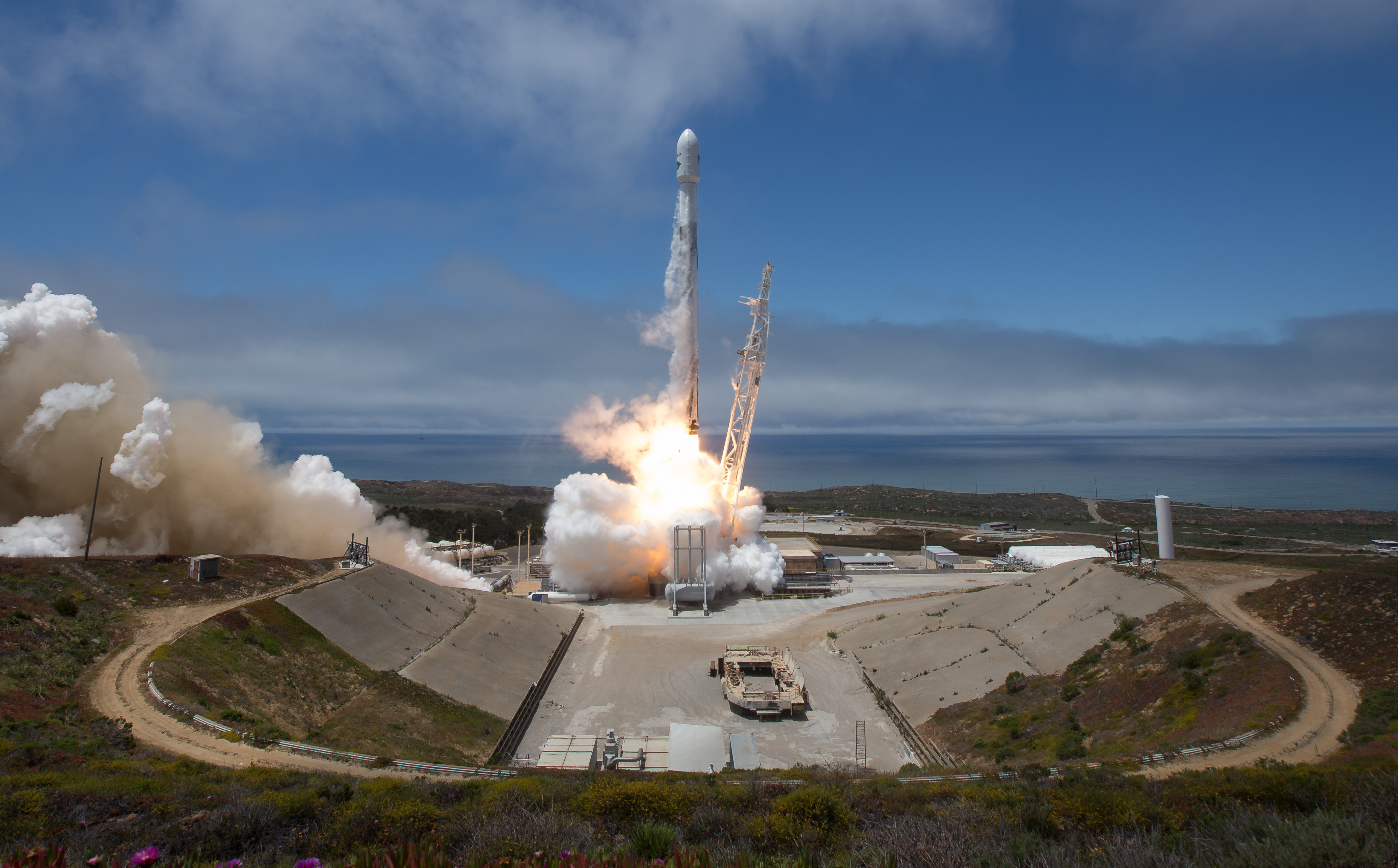 The rocket carrying GRACE-FO lifts off into a blue sky, with the Pacific Ocean beneath it.