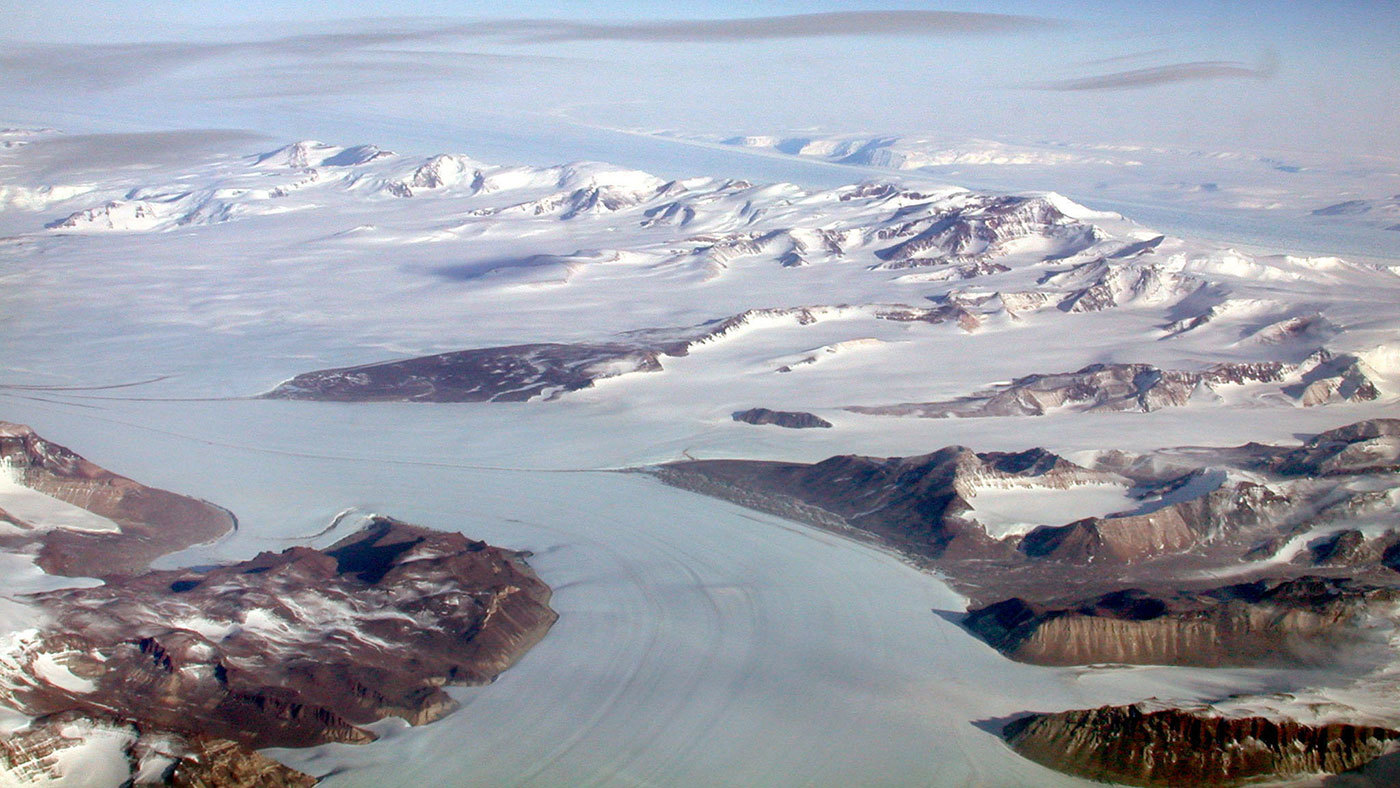 A flat area is frozen amid glaciers under a blue sky.