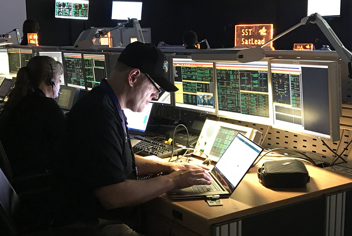 Deputy Project Manager Mike Gross sits at a computer console with multiple screens showing spacecraft status.